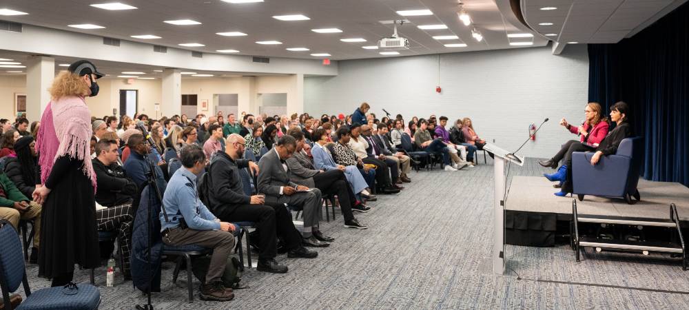 rows of people seated, two women seated on stage for presentation